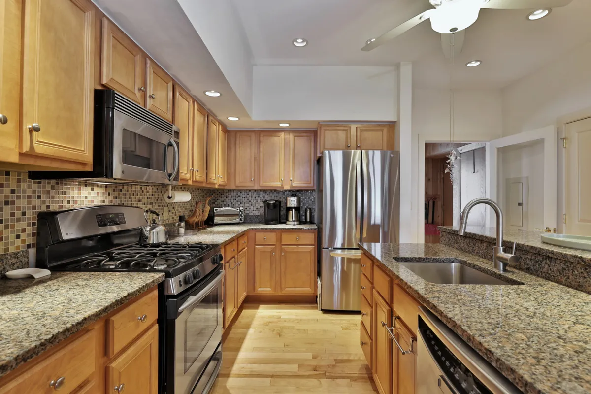 A close-up of the modern kitchen area, featuring granite countertops, stainless steel appliances, wood cabinetry, and a mosaic backsplash. The layout is ideal for preparing anything from gourmet dinners to quick breakfasts, surrounded by inviting finishes and practical design.