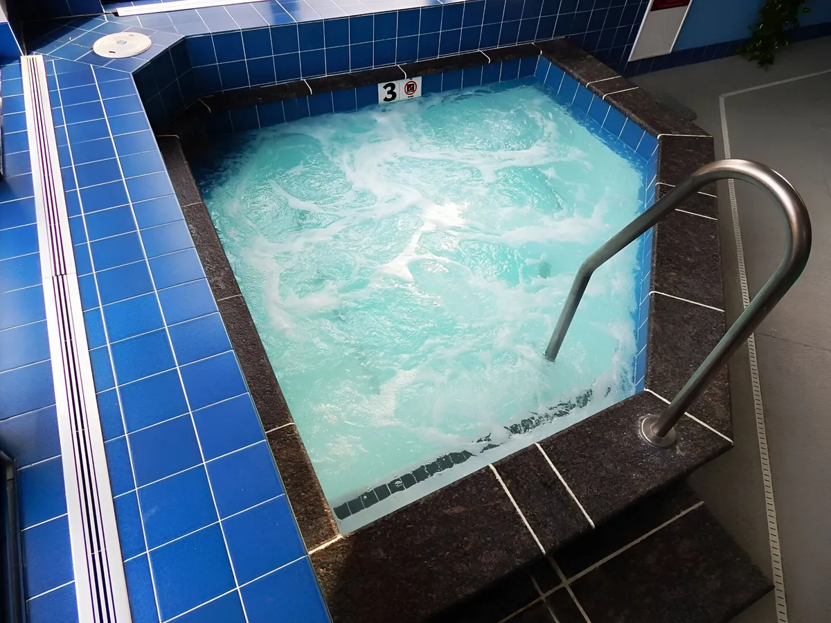 A modern jacuzzi area with blue tiles and stainless steel railings, exuding a sense of calm and relaxation. The setting is designed for unwinding, socializing, and wellness, capturing the spa-like features of the resort.