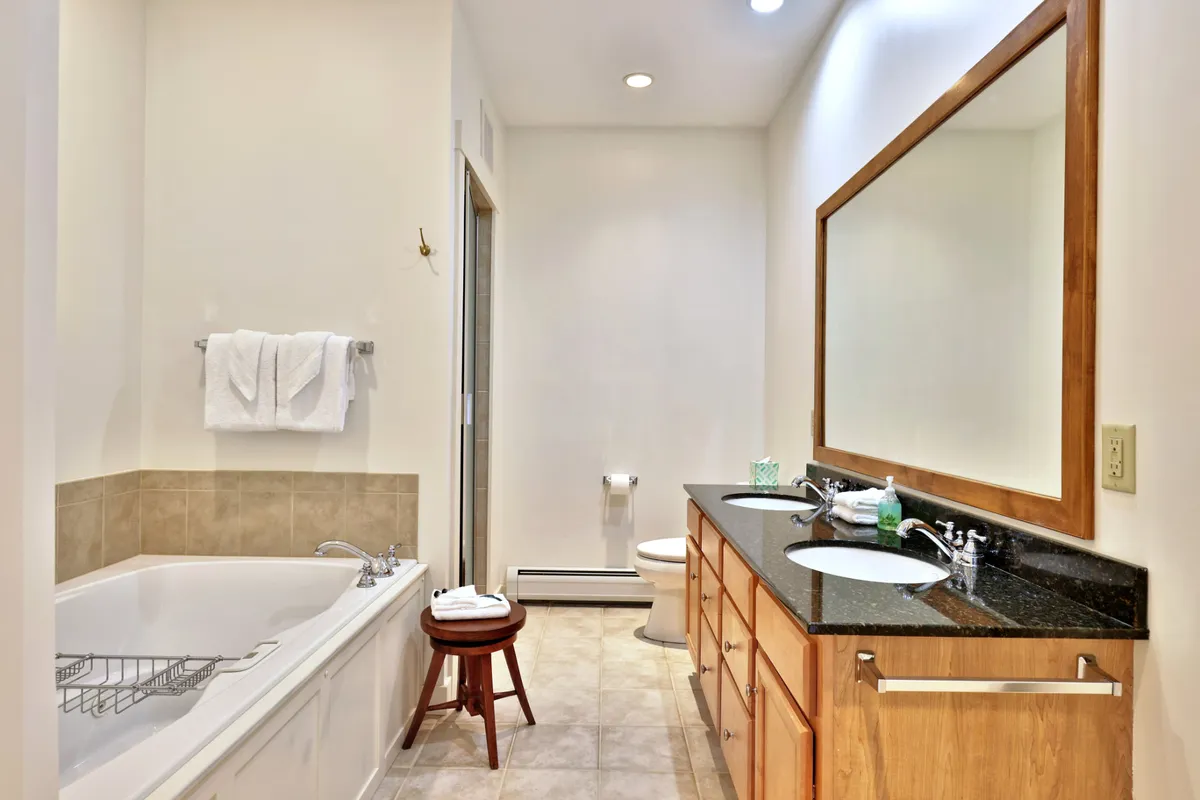 A serene bathroom with a soaking bathtub, a vanity and mirror, and a small stool. The clean lines and soft lighting evoke a spa-like environment, suggesting luxurious self-care and relaxation.