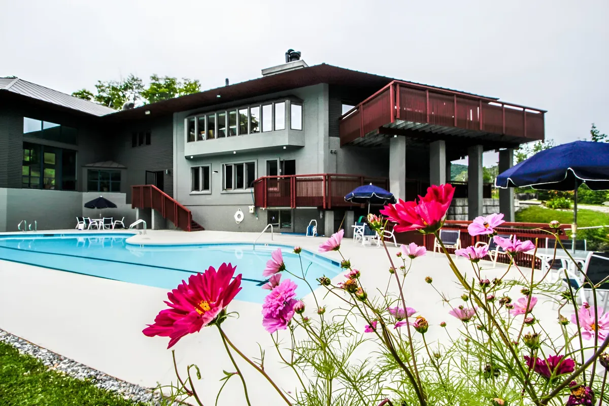 An inviting outdoor swimming pool area with flower beds, a deck, and the facade of the building visible. The setup is ideal for warm-weather gatherings, relaxation, or post-adventure socializing.