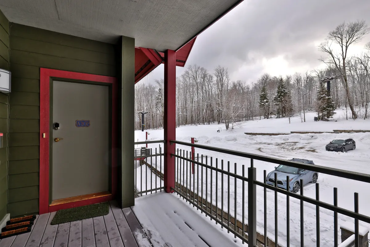 This image features the condo's front door, a snow-covered landscape, and a balcony railing, with the ambiance suggesting a peaceful winter retreat. Guests are seen enjoying the snowy view and relaxing on the balcony, setting the stage for group arrivals and après-ski gatherings.