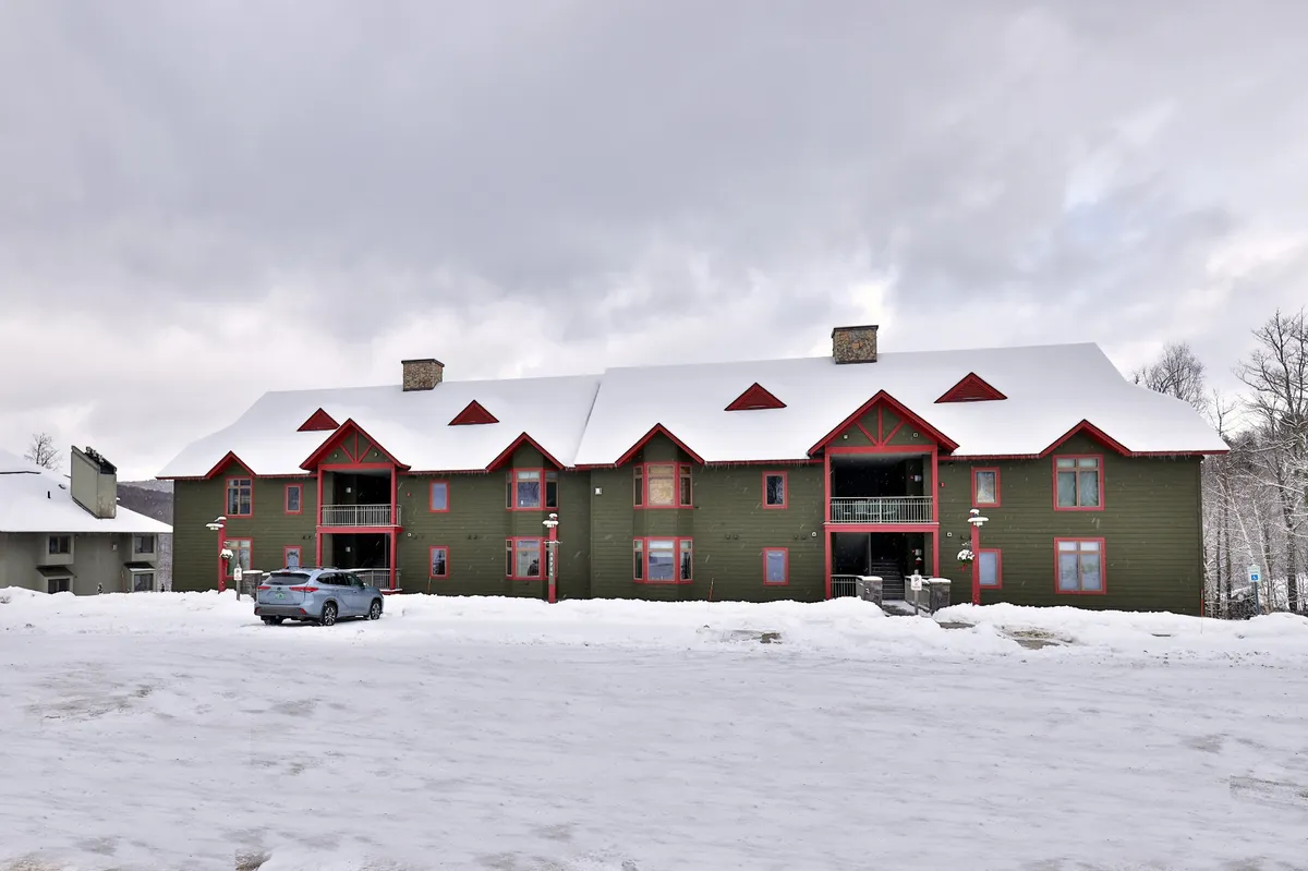 A charming exterior scene showing a snow-covered roof, red accents on the building, and a stone chimney. The mood is tranquil, inviting memories of cozy gatherings indoors after winter fun outside.