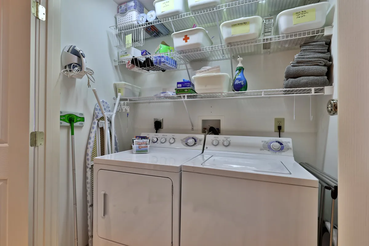 A bright and efficient laundry space equipped with a washer, dryer, ample shelving, and an ironing board. Organized storage and cleaning supplies ensure convenience for guests after days spent outdoors.