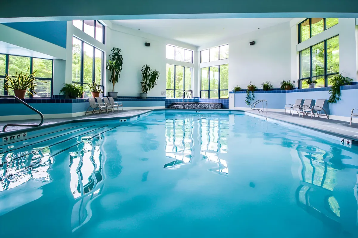 This image presents the resort's indoor swimming pool, bathed in natural light from expansive windows. Potted plants and a nearby jacuzzi create a relaxing, wellness-focused atmosphere. Lounge chairs and the spacious layout suggest a space for both active recreation and quiet relaxation.
