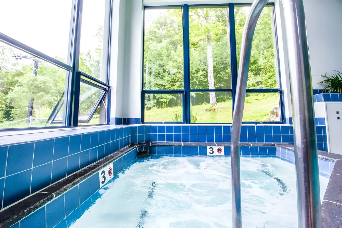 A calming interior scene featuring a spacious indoor hot tub area with large windows overlooking natural surroundings dusted with snow. The space is perfect for relaxing and socializing after a day on the slopes, echoing the rejuvenating amenities mentioned in the section.