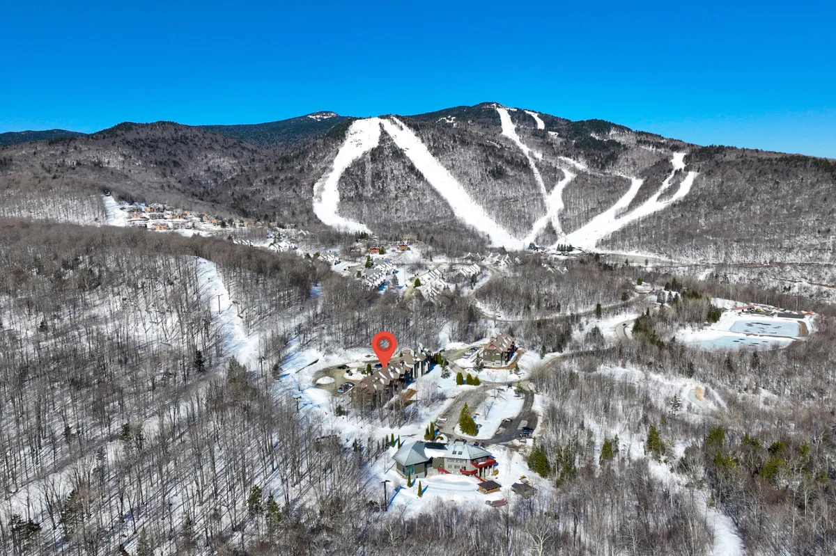 A sweeping view of snow-covered mountains, ski slopes, residential properties, and a forested area. The picture captures the excitement of nearby resort life and the allure of evening or sunrise gatherings after a day on the slopes.